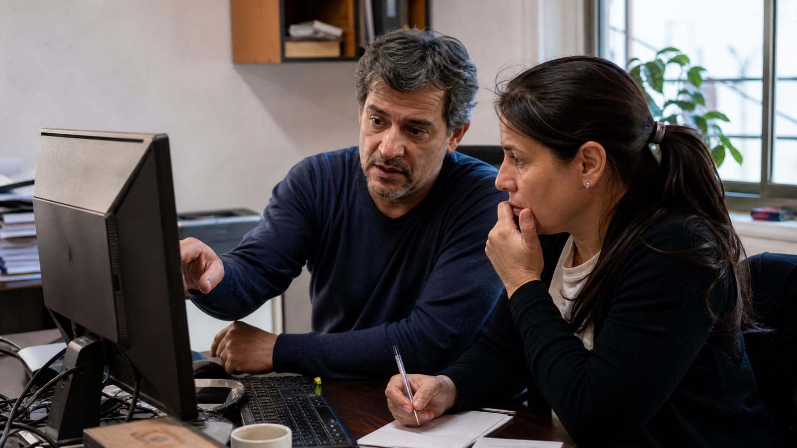 Dos personas revisando información en una computadora de escritorio en una oficina